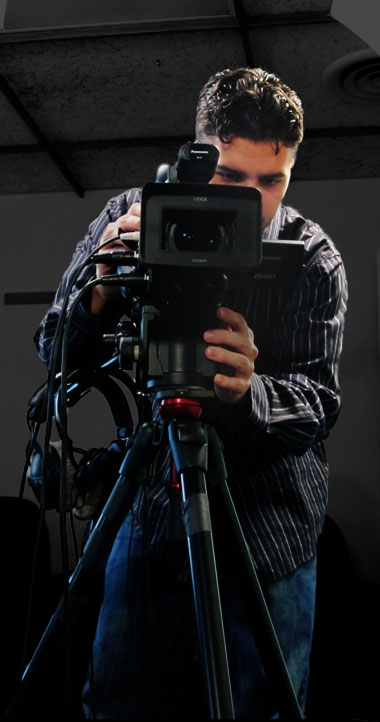 Full body photo of Ryan operating a digital video camera mounted on a tripod.